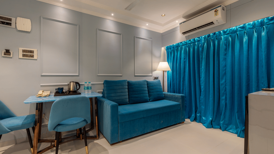 A cosy living area with a blue couch, a small dining table with chairs, and blue drapes - Home2 Residency, Mumbai Airport