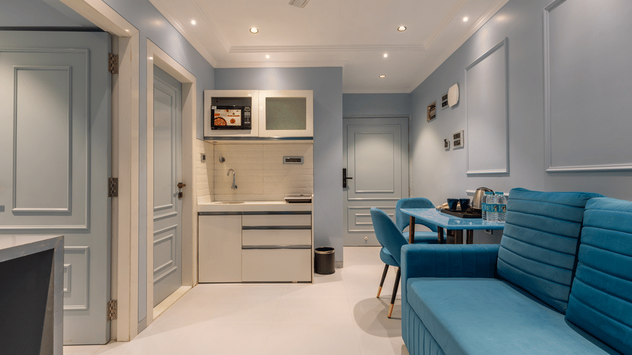An integrated studio space featuring a modern kitchenette, dining table with blue chairs, and a matching blue sofa - Home2 Residency, Mumbai Airport