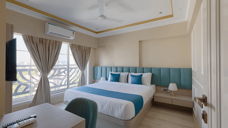 A well-lit deluxe bedroom with a queen bed, turquoise accents, and a large window with curtains - Home2 Residency, Mumbai Airport