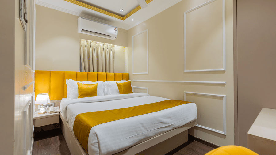 A comfortable double bed with a bright yellow headboard, white linens, and warm ambient lighting - Home2 Residency, Mumbai Airport