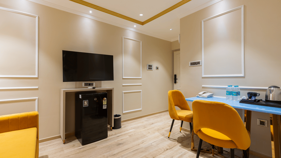 Interior view of a room featuring a wall-mounted TV, work desk, and vibrant yellow seating - Home2 Residency, Mumbai Airport
