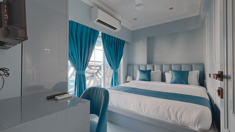 A bright bedroom featuring a queen bed with blue accents, a work desk, and vibrant blue curtains - Home2 Residency, Mumbai Airport