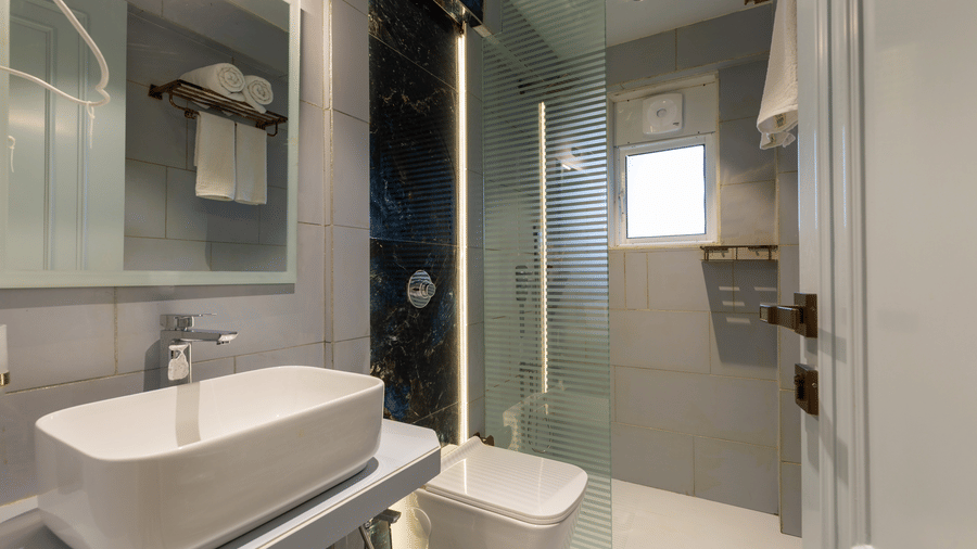 A contemporary bathroom with a white vessel sink, glass shower door, and soft grey wall panels - Home2 Residency, Mumbai Airport