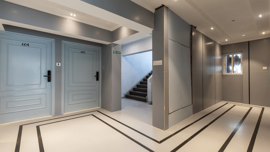 A sleek hotel hallway featuring light blue room doors, polished white flooring with black accents, and a staircase - Home2 Residency, Mumbai Airport