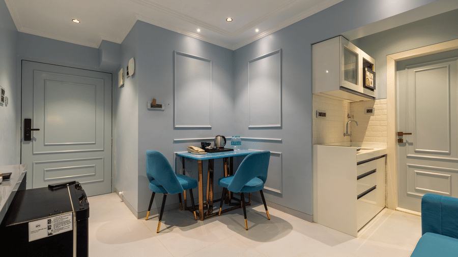 An open-plan studio layout showing a blue dining set, kitchenette, and entryway - Home2 Residency, Mumbai Airport