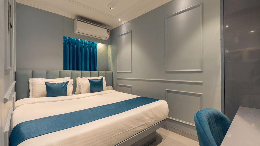 A neatly arranged bedroom with blue decorative pillows and a matching bed runner under soft lighting - Home2 Residency, Mumbai Airport