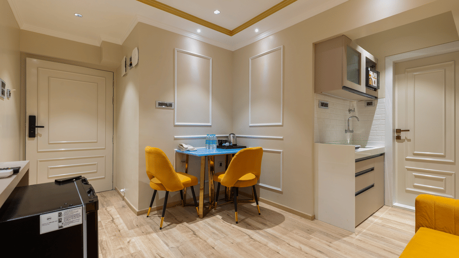 A compact studio apartment layout with a small dining table, yellow chairs, and a kitchenette - Home2 Residency, Mumbai Airport