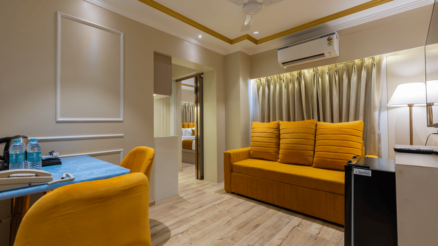 Wide view of a studio apartment showing a yellow seating area and entry to the bedroom - Home2 Residency, Mumbai Airport