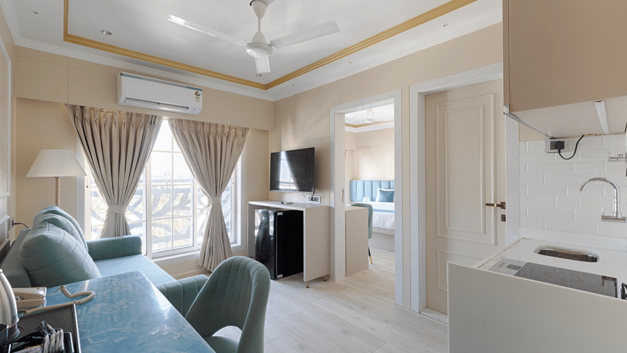 A multi-functional living space with a teal sofa, dining chairs, and a visible kitchenette - Home2 Residency, Mumbai Airport