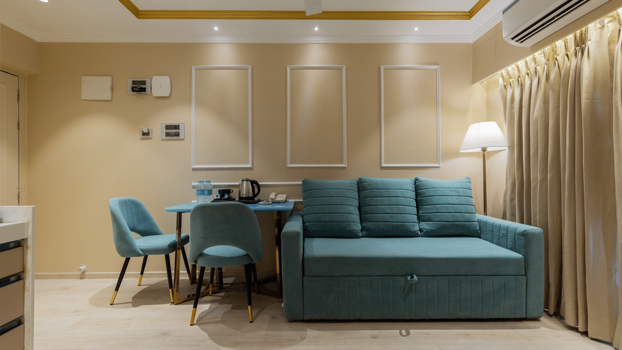 Modern interior with a plush teal sofa bed and a small dining set for two - Home2 Residency, Mumbai Airport