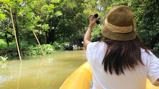 A woman rafting through a water body with lush green forest on either side.
