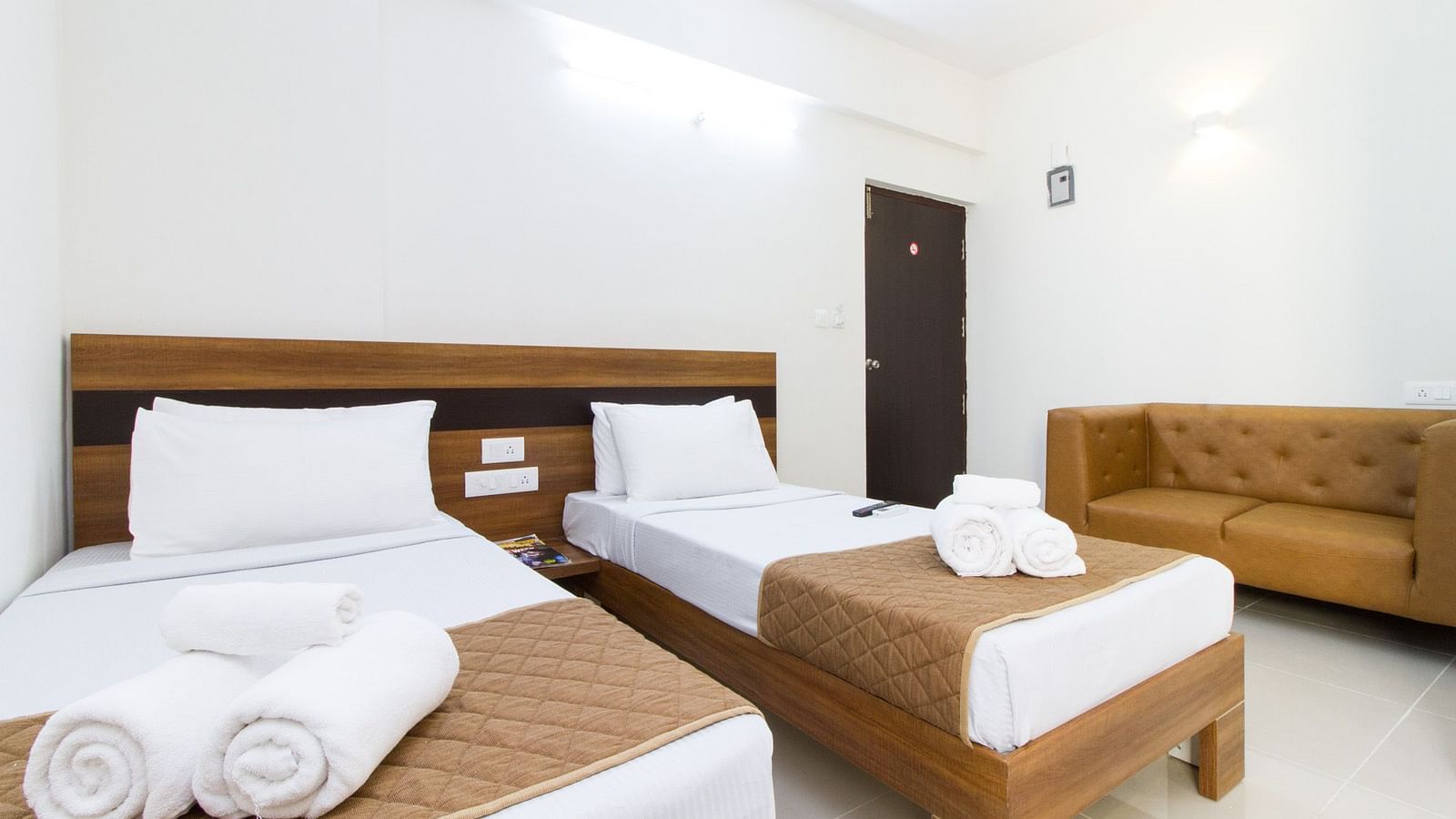 A room at Sanctum Suites Whitefield, Bangalore including twin beds with brown and white bedding and a sofa.