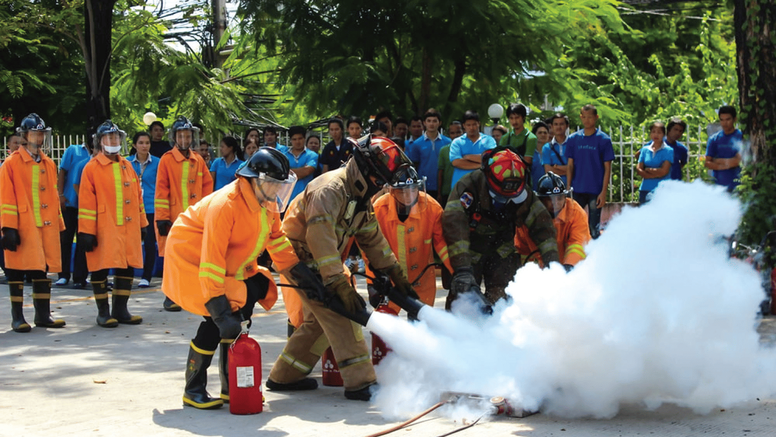 Firefighters in protective gear demonstrating fire extinguisher usage during a safety drill in front of a crowd at Water Kingdom.