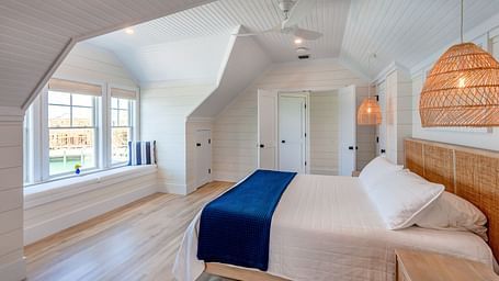 Bedroom with sloped ceilings, blue bed runner, and woven pendant light | Abaco Inn