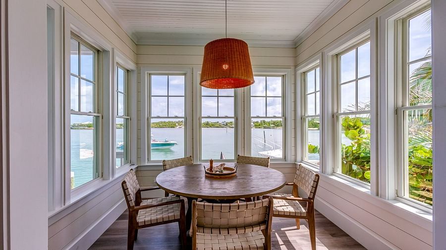 Dining nook with a round wooden table, wicker chairs, and large windows overlooking greenery | Abaco Inn