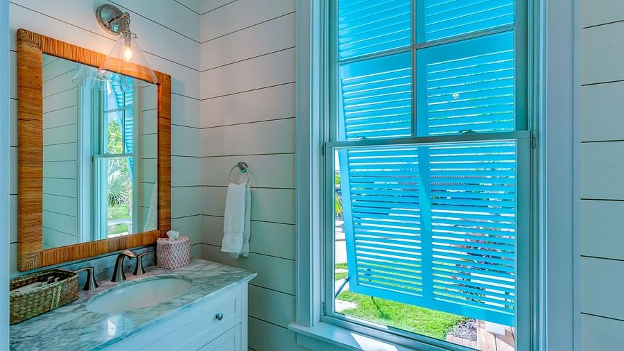 Bathroom with white vanity, wooden mirror frame, and window with blue shutters | Abaco Inn