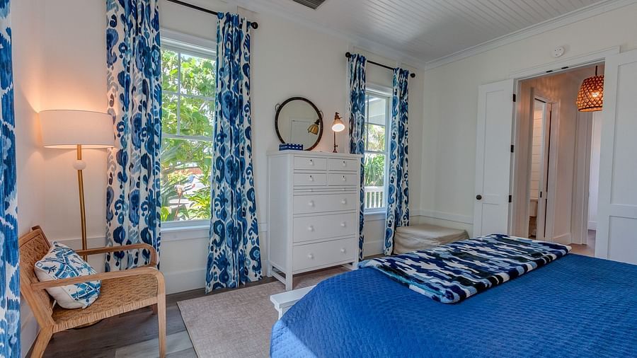 Bedroom with blue curtains, a wooden chair, and a cozy bed | Abaco Inn