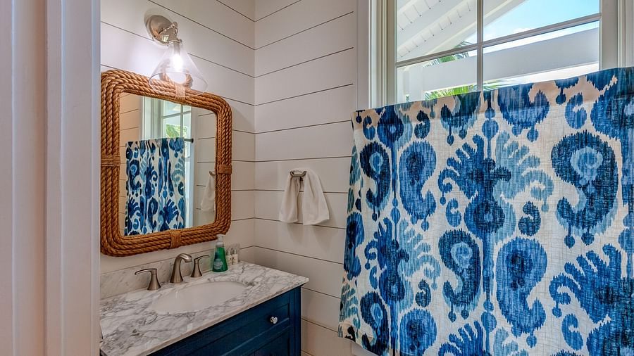 Bathroom with a white vanity, a mirror with a wooden frame, and blue paisley shower curtain | Abaco Inn