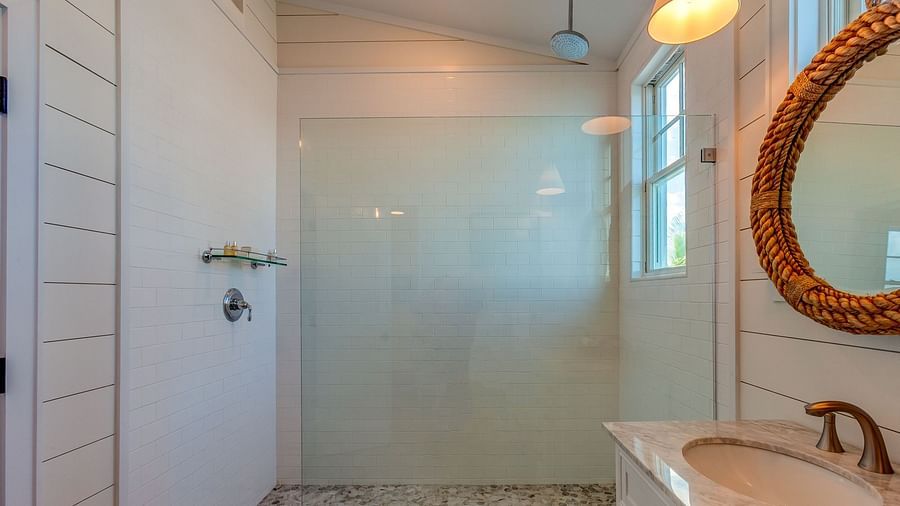 Bathroom with a glass shower, marble flooring, and a woven mirror | Abaco Inn