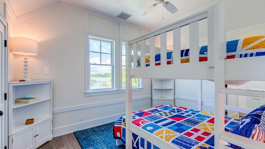 Bunk bed room with colorful bedding, a white dresser, and a window | Abaco Inn