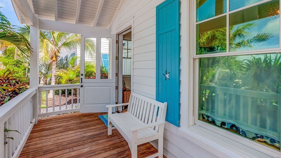 Wooden porch with a white chair next to a turquoise door and window | Abaco Inn