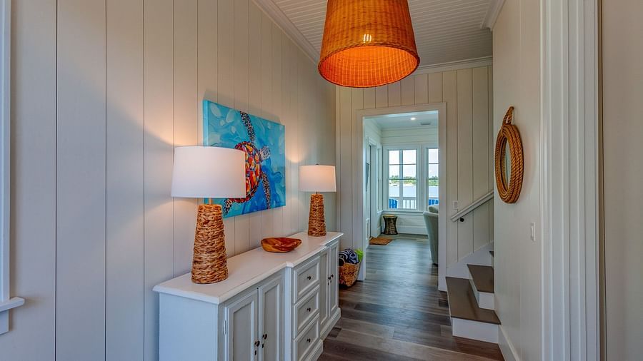Hallway with a white sideboard, lamp, and artwork leading to a door | Abaco Inn