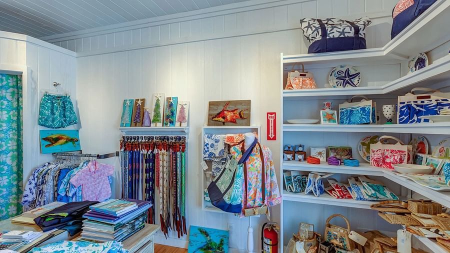 Boutique showcasing beach-style clothing and accessories, including bags and souvenirs displayed across multiple shelves.