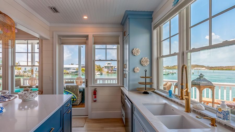 Bright, airy , white and blue coloured theme kitchen with golden taps and windows that overlooks the sea at Abaco Inn.
