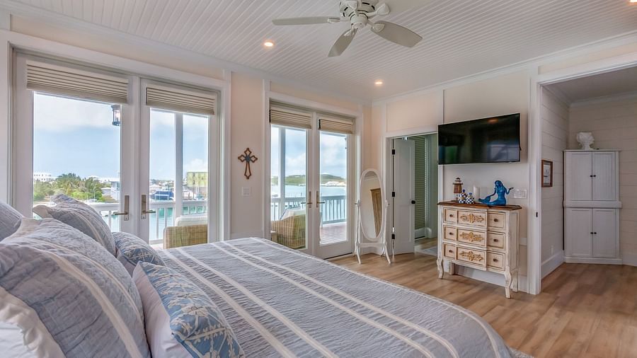 A bright, airy bedroom with a huge bed, TV, cupboard, wardrobe, Ceiling fan and glass doors  that overlooks the sea at Abaco Inn.