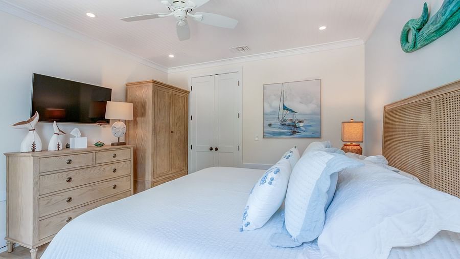 A bedroom with a huge bed with blue comforter, cupboards, TV, and wall arts at Abaco Inn.