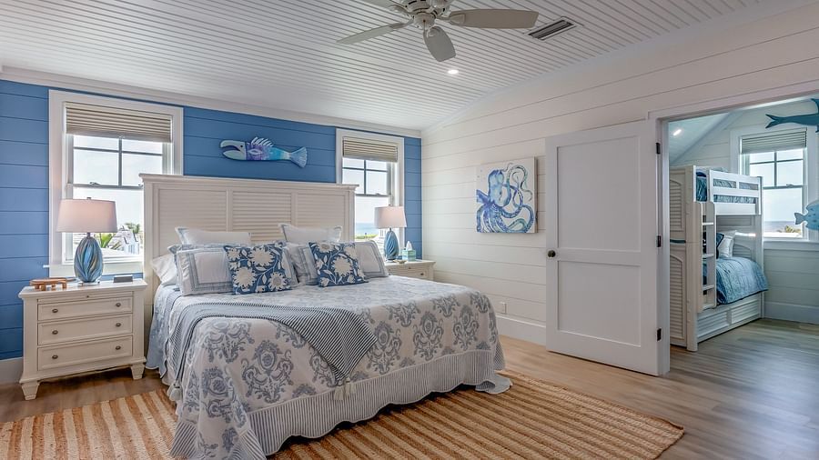 a blue and white themed, spacious bedroom with a huge bed, bedside drawers, wall arts, ceiling fan, windows, and a door that leads to a room with bunk bedsat Abaco Inn. 