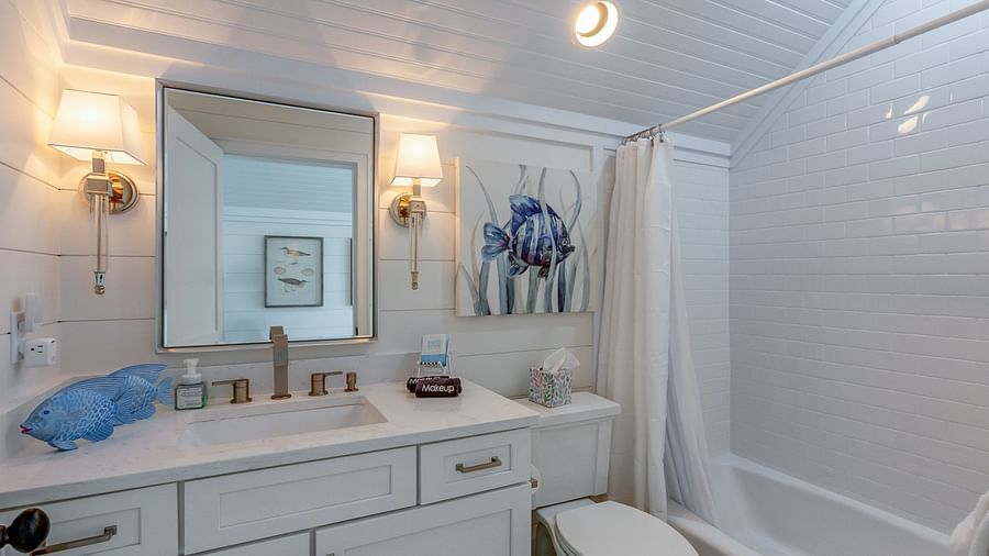 a bathroom with a curtained bathtub, a commode, a mirror and a sink with drawers at Abaco Inn.
