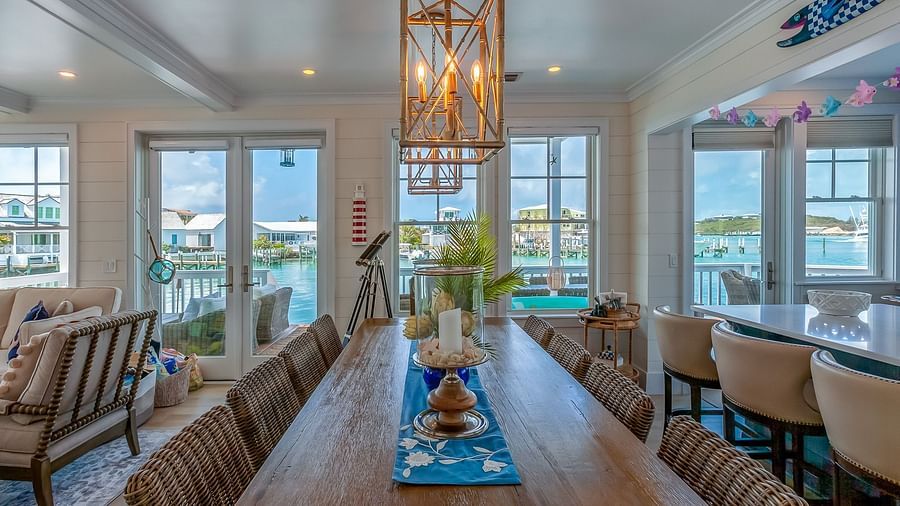 a wooden table with multiple chairs surrounding it and windows that overlook the sea.