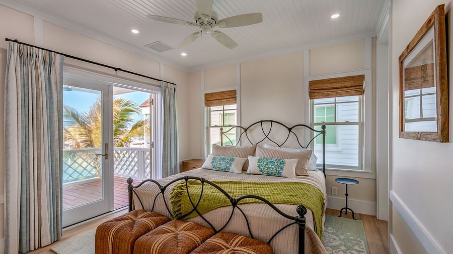 Well lit spacious bedroom with a huge bed on a decorative rug, ceiling fan, windows and a sliding glass door leading to the balcony with a sea view at Abaco Inn.