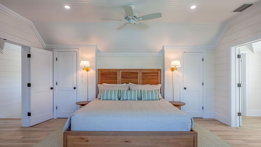 A spacious bedroom with a huge bed, ceiling fan, lamps and wooden doors at Abaco Inn.