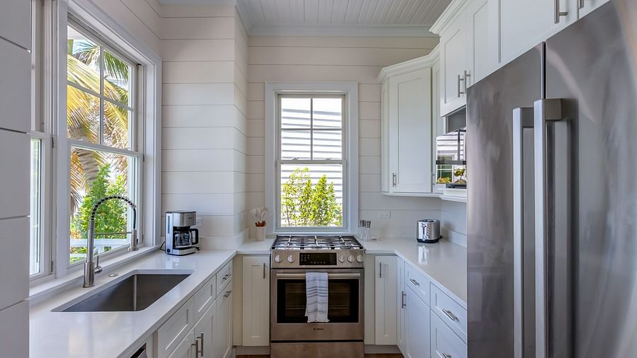 Bright and airy kitchen with a sink, oven, chimney, cupboards and windows overlooking greenery at Abaco Inn.