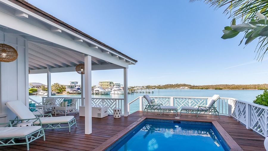 Private poolside deck with sun loungers and seating, overlooking a coastal bay with docked boats and distant hills at Abaco Inn