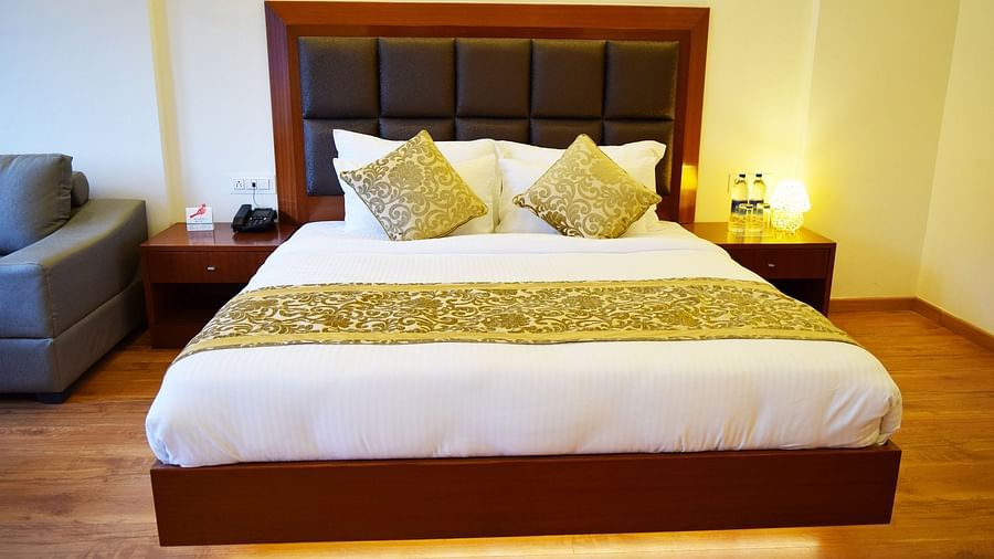 The image shows a hotel room with a large bed, two nightstands, and a couch in the background  | DLS Serenity Resort and Spa