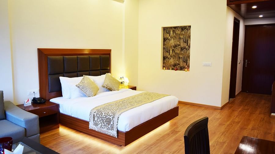 The image shows a hotel room with a large bed, two nightstands, and a couch in the background  | DLS Serenity Resort and Spa