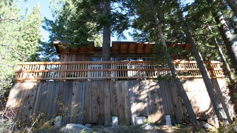 A rustic cabin with weathered wood siding and a roof nestled among tall trees. - Kit Carson Lodge