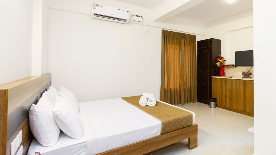 A neatly arranged hotel bedroom with a double bed, dark wood furniture, white walls, and a ceiling fan