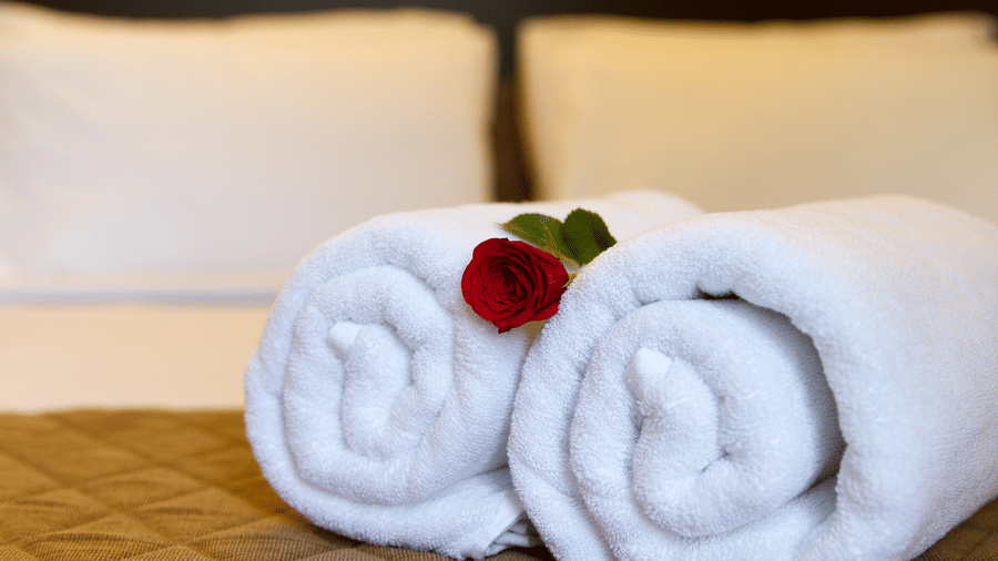 Close-up of neatly folded white towels with a red rose on a hotel bed at Sanctum Suites Whitefield, Bangalore.