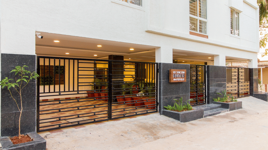 Hotel entrance exterior with manicured landscaping, potted plants, and a well-lit façade at Sanctum Suites Whitefield, Bangalore.