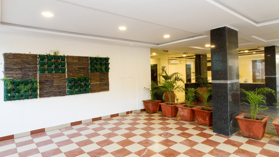 Hotel lobby with a checkered tile floor, dark pillars, and potted plants at Sanctum Suites Whitefield, Bangalore.