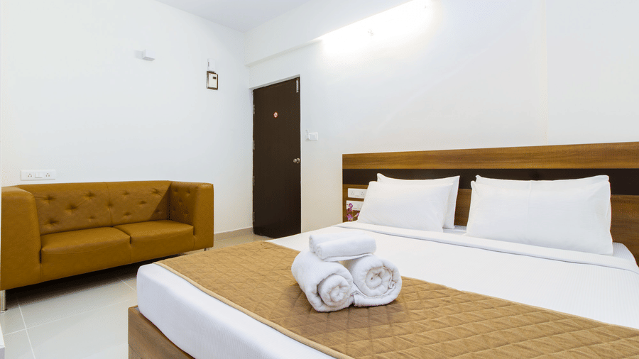 Hotel room with a double bed, white linen, an air conditioner, and a wooden wardrobe at Sanctum Suites Whitefield, Bangalore.