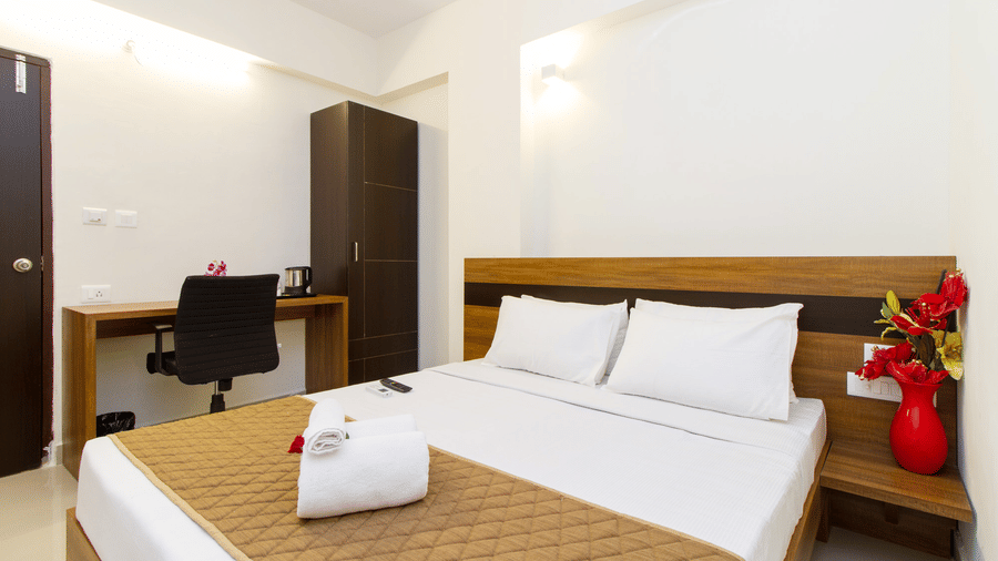 Hotel room with a double bed, a study chair, and a red vase accent at Sanctum Suites Whitefield, Bangalore.