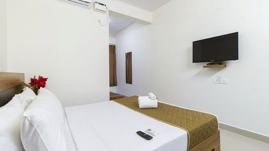 Hotel room with a double bed, a wall-mounted television, and a red floral accent at Sanctum Suites Whitefield, Bangalore.