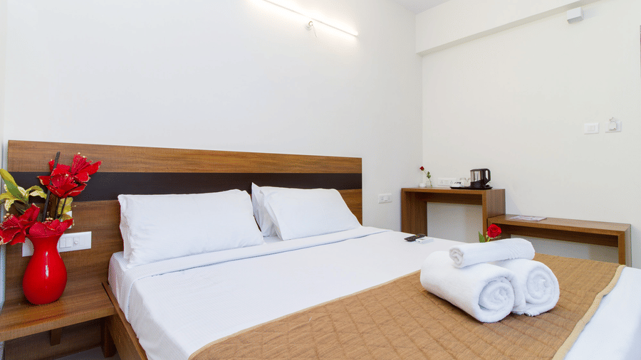 Hotel room with a double bed, white linen, neatly folded towels, and a red rose vase at Sanctum Suites Whitefield, Bangalore.