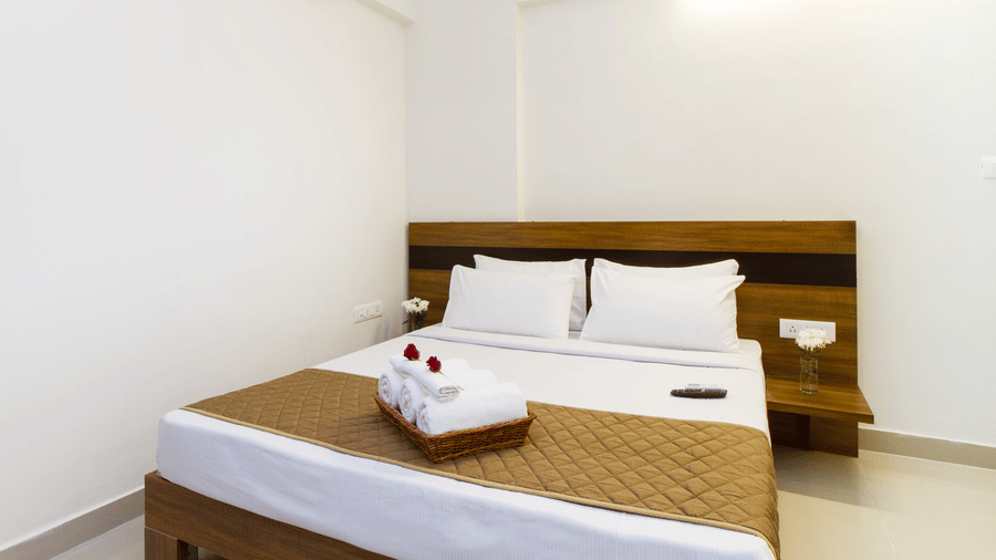 Wide-angle view of a hotel room with a double bed, white linen, and floral accents at Sanctum Suites Whitefield, Bangalore.