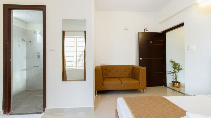 Hotel room entrance with a full-length mirror, a sofa, and a wooden door at Sanctum Suites Whitefield, Bangalore.